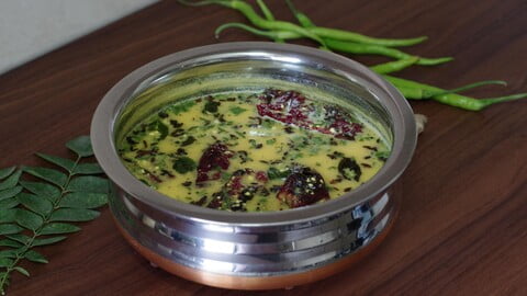 Gujarathi Kadhi in a bowl next to green chilies and curry leaves