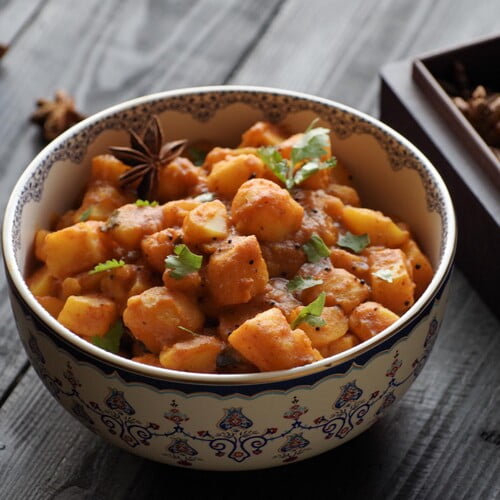 Batata nu shaak - Gujarati potato curry in a painted bowl on a black board next to spices