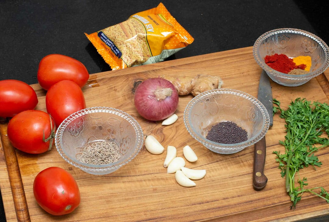 Zutaten für Sev Tameta nu Shaak - Ingredients for tameta nu shaak on a wooden chopping board