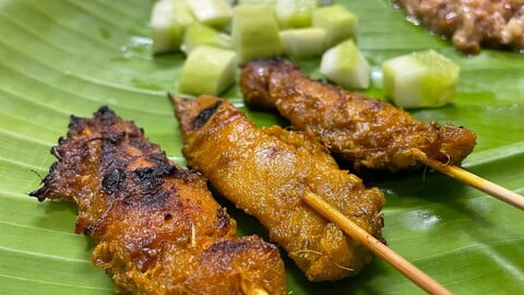 Hähnchen Satay auf einem Bananenblatt mit Gurke, Reis und Erdnusssauce - Chicken Satay on a banana leaf together with cucumber, rice and peanut sauce