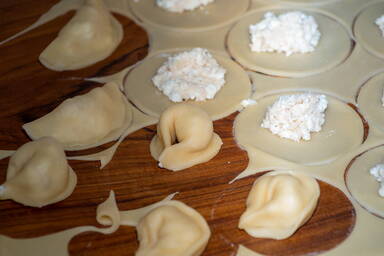 Füllung auf runden, ausgestochenen Nudeln neben bereits fertigen Cappelletti - Filling on round cut out pasta next to already finished cappelletti.