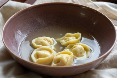 Cappelletti gefüllt mit Hähnchenbrust in Hühnerbrühe in einer lila Schüssel - Cappelletti stuffed with chicken breast in chicken broth in a purple bowl