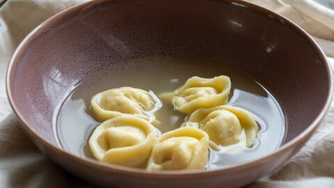 Cappelletti gefüllt mit Hähnchenbrust in Hühnerbrühe in einer lila Schüssel - Cappelletti stuffed with chicken breast in chicken broth in a purple bowl