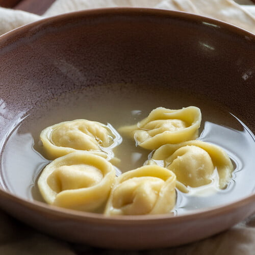 Cappelletti gefüllt mit Hähnchenbrust in Hühnerbrühe in einer lila Schüssel - Cappelletti stuffed with chicken breast in chicken broth in a purple bowl