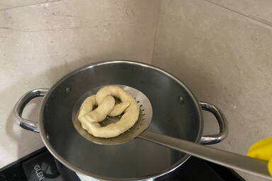 Abtropfen der Brezellauge über dem Topf mit Schaumkelle und Handschuhen - Straining the lye from the pretzel over the pot, using a strainer spoon and gloves