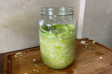 Einmachglas mit frisch gestampftem Kraut und Salzlake mit einem Kohlblatt abgedeckt - Canning jar with freshly mashed cabbage and brine covered with a cabbage leaf