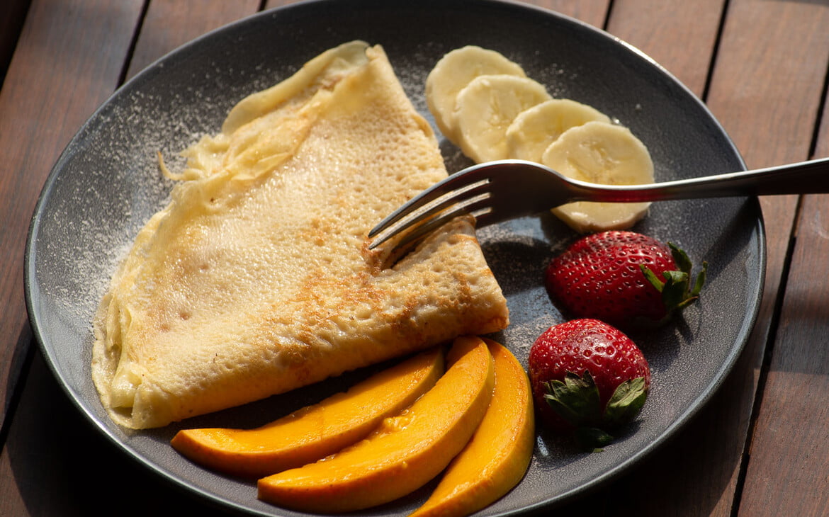 Crêpe mit Puderzucker und frischem Obst auf einem Teller angerichtet - Plated Crêpe with powdered sugar and fresh fruit