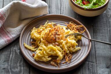 Käsespätzle mit Röstzwiebeln neben einer kleinen Schüssel Salat - Spaetzle with melted cheese next to a small side salad in a bowl