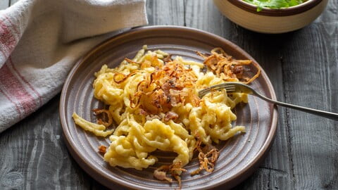 Käsespätzle mit Röstzwiebeln neben einer kleinen Schüssel Salat - Spaetzle with melted cheese next to a small side salad in a bowl