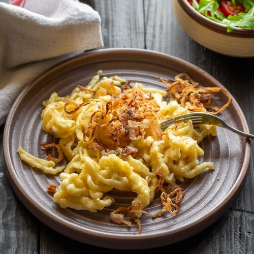 Käsespätzle mit Röstzwiebeln neben einer kleinen Schüssel Salat - Spaetzle with melted cheese next to a small side salad in a bowl