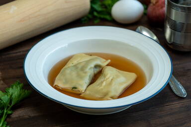 Maultaschen in Brühe in einem Teller mit blauem Rand neben einem rohen Ei und Petersilie - Maultaschen in broth in a bowl with a blue rim next to a raw egg and parsley