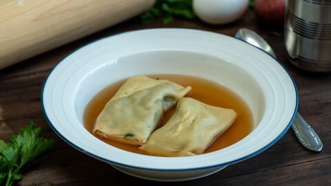 Maultaschen in Brühe in einem Teller mit blauem Rand neben einem rohen Ei und Petersilie - Maultaschen in broth in a bowl with a blue rim next to a raw egg and parsley