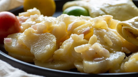 SÜddeutscher Kartoffelsalat auf einem Teller, zusammen mit Kirschtomaten in gelb, grün und rot, neben angebratenen Maultaschen - Southern German Potato Salad on a dark plate next to cherry tomatoes in green, yellow and red together with fried up Maultaschen