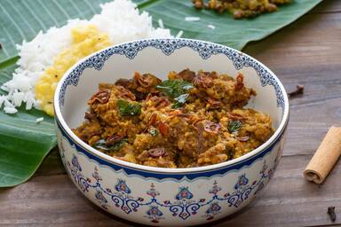 Beef Varutharacha Curry in einer verzierten Schüssel vor einem Bananenblatt mit Reis und Dal - Beef Varutharacha Curry in a decorated bowl in front of a banana leaf with rice and dal