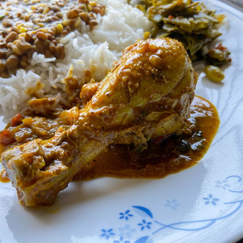 Kozhi Curry auf einem Teller mit Reis, Dal und Bohnengemüse - Kozhi Curry on a plate next to rice, dal and green beans