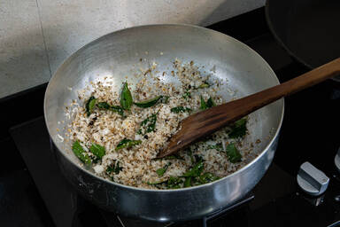 Geriebene Kokosnuss mit Curryblättern und Gewürzen auf dem Herd - Grated coconut together with curry leaves and spices on the stove