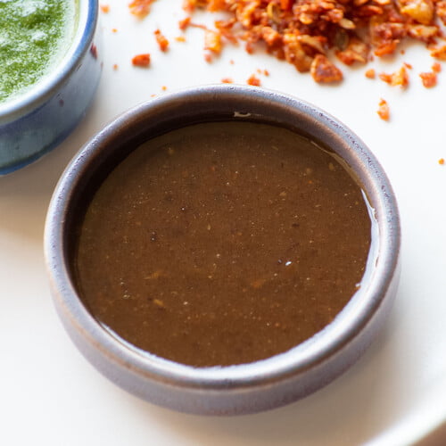 Indisches süßes Chutney in einer kleinen Schale, dahinter grünes Chutney und trockenes Knoblauchchutney - Indian sweet chutney in a small bowl, in the background green chutney and dry garlic chutney