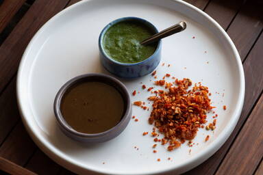 Indisches, trockenes Knoblauchchutney, grünes Chutney und süßes Chutney in kleinen Schalen auf einem weißen Teller - Indian dry garlic chutney, green chutney and sweet chutney in small bowls on a white plate