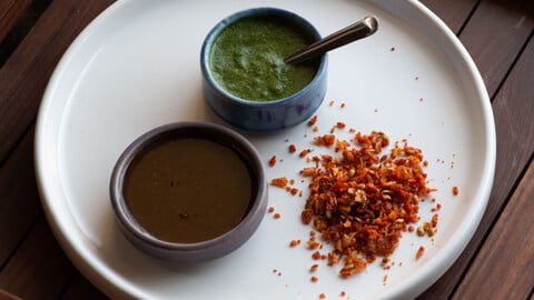 Indisches, trockenes Knoblauchchutney, grünes Chutney und süßes Chutney in kleinen Schalen auf einem weißen Teller - Indian dry garlic chutney, green chutney and sweet chutney in small bowls on a white plate