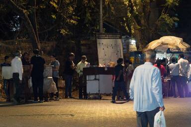 Typische Szene in Mumbai am Abend: mehrere Streetfood- (Chaat-) Händler nebeneinander mit Kunden - typical scene in Mumbai in the evening: three streetfood vendors (chaatwalas) next to each other with their customers