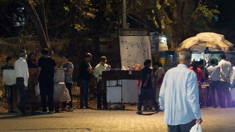 Typische Szene in Mumbai am Abend: mehrere Streetfood- (Chaat-) Händler nebeneinander mit Kunden - typical scene in Mumbai in the evening: three streetfood vendors (chaatwalas) next to each other with their customers