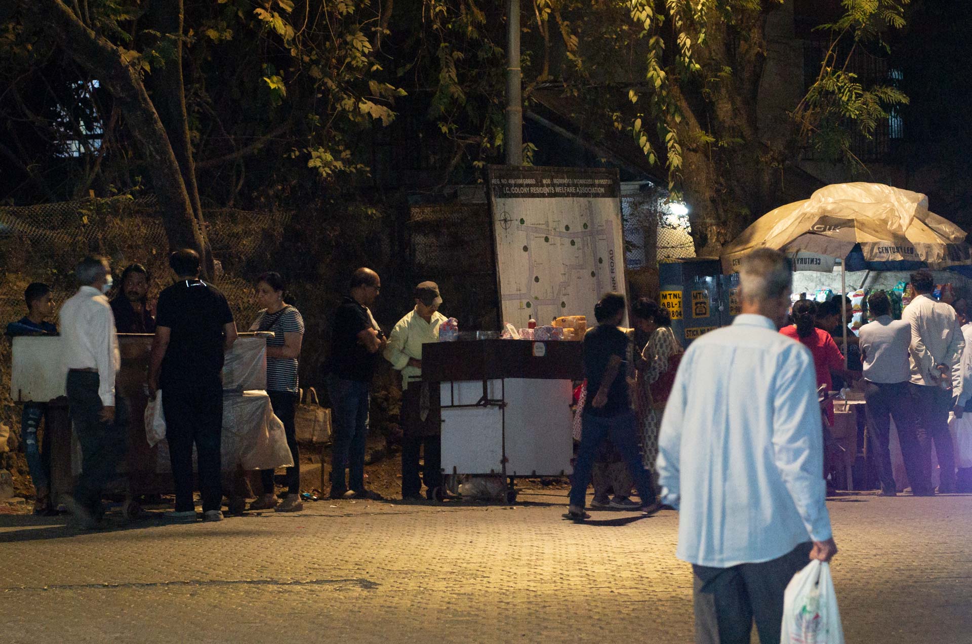 Typische Szene in Mumbai am Abend: mehrere Streetfood- (Chaat-) Händler nebeneinander mit Kunden - typical scene in Mumbai in the evening: three streetfood vendors (chaatwalas) next to each other with their customers
