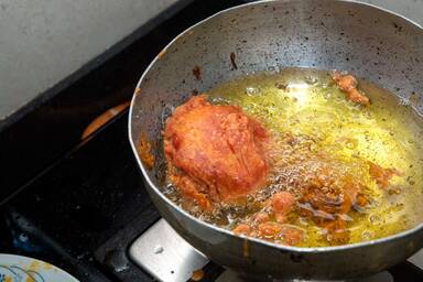 Batata Vada beim Fritieren im heißen Öl in einem Topf auf dem Herd - Batata vada deep frying in oil in a pot on the stove