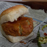 Batata Vada in a Pav with fried green chilies on the side on a newspaper