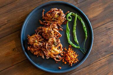 Zwiebel-Pakoras auf einem schwarzen Teller zusammen mit Knoblauchchutney und frittierten grünen Chilis - Onion pakoras on a black plate along with garlic chutney and fried green chilies