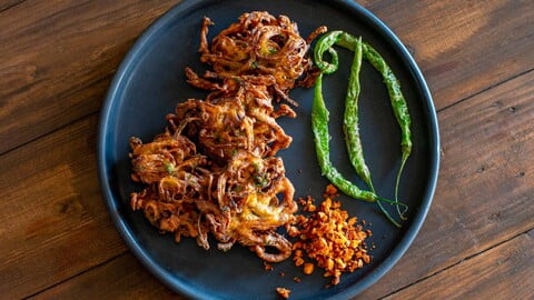 Zwiebel-Pakoras auf einem schwarzen Teller zusammen mit Knoblauchchutney und frittierten grünen Chilis - Onion pakoras on a black plate along with garlic chutney and fried green chilies