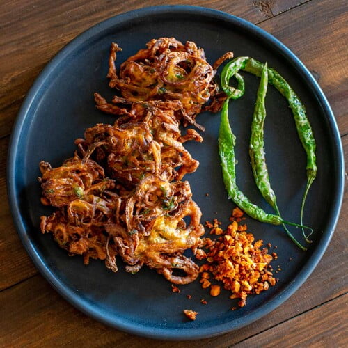 Zwiebel-Pakoras auf einem schwarzen Teller zusammen mit Knoblauchchutney und frittierten grünen Chilis - Onion pakoras on a black plate along with garlic chutney and fried green chilies