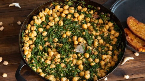 Espinacas con garbanzos in der Pfanne neben einem schwaren Teller mit in Olivenöl gebratenem Brot - Espinacas con garbanzos in the pan next to a black plate with bread fried in olive oil