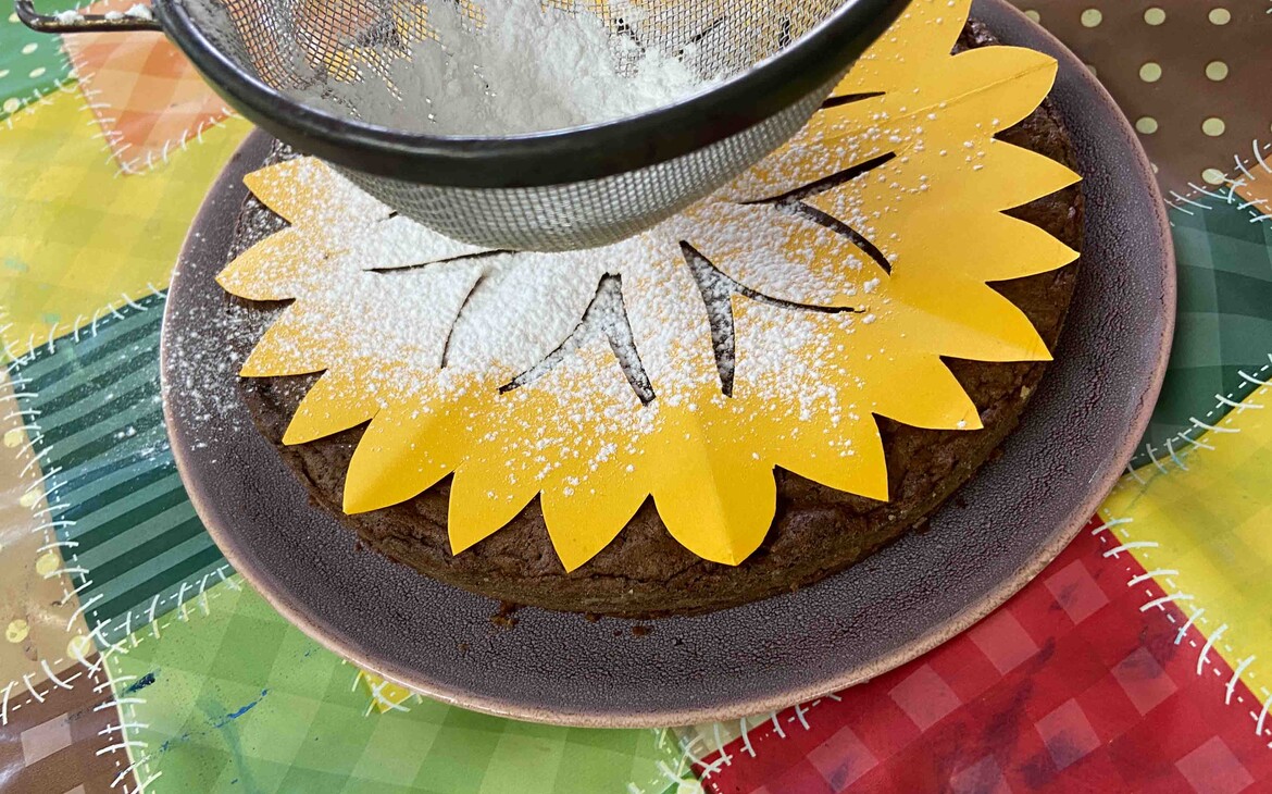 Chocolate cake with stencil cut out while decorating with powdered sugar