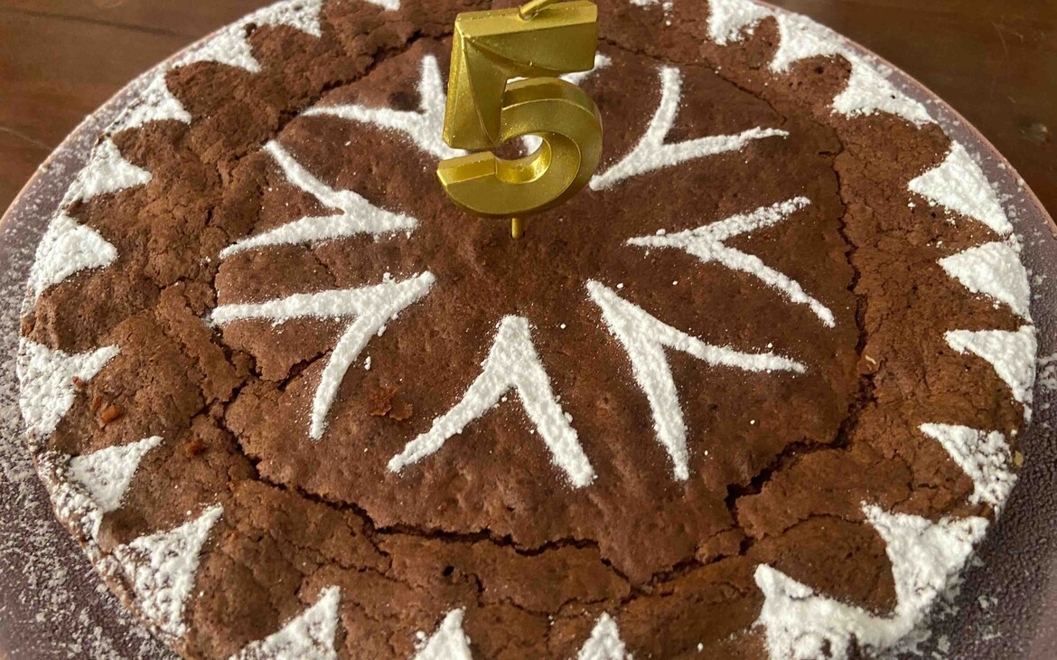 Lorraine chocolate cake with almond flour, with a pattern of sprinkled powdered sugar and a birthday candle in the center