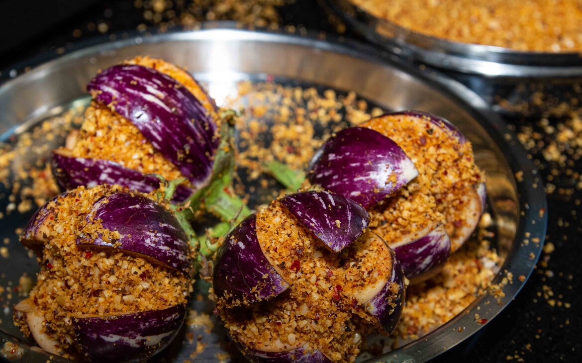 4 peanut-stuffed eggplants before frying on a plate next to a bowl with the filling