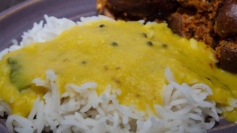 Vatpachi Dal - ein gelbes Toor Dal über eine Portion Reis gegossen, neben kleinen, mit Erdnüssen gefüllte Auberginen auf einem Teller angerichtet - Vatpachi Dal - a yellow toor dal poured over a portion of rice, arranged on a plate next to small eggplants stuffed with peanuts