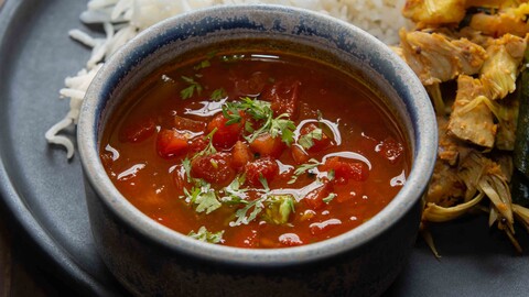 Tomatenrasam in einer kleinen blauen Schüssel auf einem Teller mit Gemüse und Reis - Tomato rasam in a small blue bowl on a plate with vegetables and rice